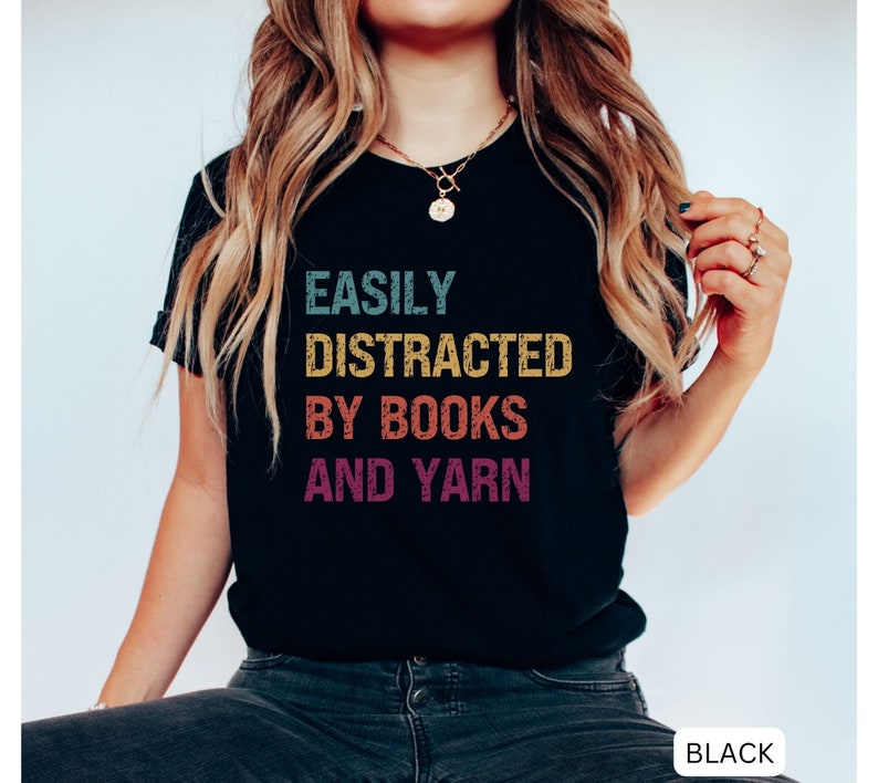 May include: Black t-shirt with the text "EASILY DISTRACTED BY BOOKS AND YARN" in a rainbow color scheme.