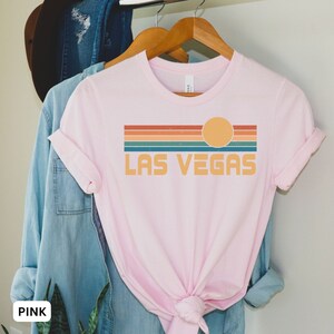 May include: Pink t-shirt with a retro-style graphic of a sunset over the text "LAS VEGAS".