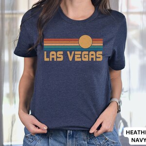 May include: A heather navy blue t-shirt with a retro sunset graphic and the text "LAS VEGAS" in yellow.