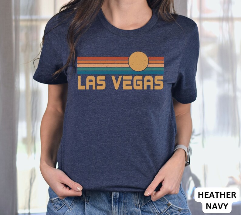 May include: A heather navy blue t-shirt with a retro sunset graphic and the text "LAS VEGAS" in yellow.