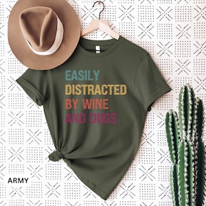 May include: A green t-shirt with the text "EASILY DISTRACTED BY WINE AND DOGS" in a vintage style font. The text is in different colors, including yellow, orange, red, and purple.