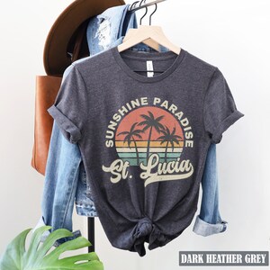 May include: Dark heather grey t-shirt with a vintage-style graphic of palm trees and a sunset. The graphic says "Sunshine Paradise St. Lucia".