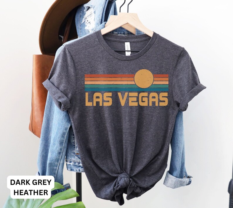 May include: Dark grey heather t-shirt with a retro-style graphic of a sunset over a striped horizon with the text "LAS VEGAS".