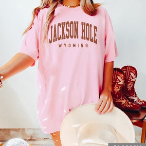 May include: A pink t-shirt with the text "JACKSON HOLE WYOMING" in brown letters.