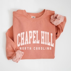 May include: A coral colored sweatshirt with the text "Chapel Hill North Carolina" in white.