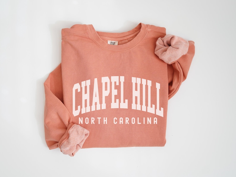May include: A coral colored sweatshirt with the text "Chapel Hill North Carolina" in white.