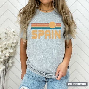 May include: A gray t-shirt with a retro-style graphic of a sunset over the word "SPAIN" in orange.