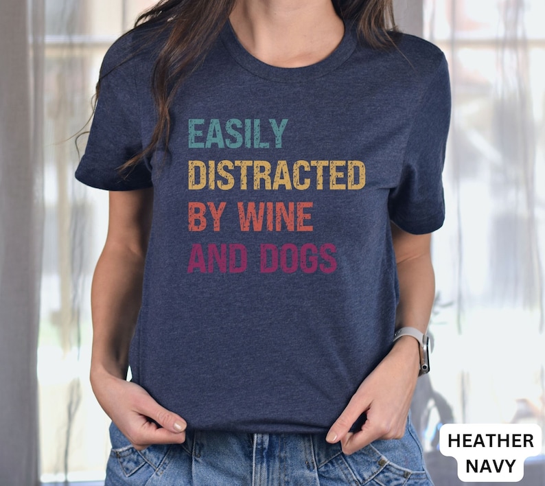 May include: A heather navy blue t-shirt with the text "EASILY DISTRACTED BY WINE AND DOGS" in a vintage style font.