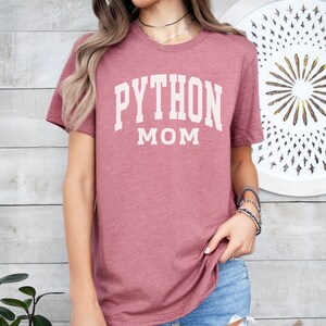 Peut inclure: Un t-shirt mauve avec le texte "PYTHON MOM" en blanc.