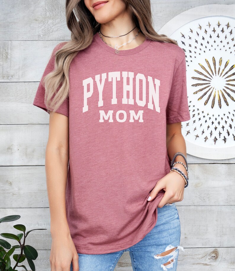 Peut inclure: Un t-shirt mauve avec le texte "PYTHON MOM" en blanc.