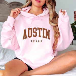 May include: Light pink hooded sweatshirt with the text "AUSTIN TEXAS" in brown lettering.