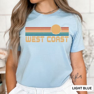 May include: Light blue t-shirt with a retro sunset graphic and the text "WEST COAST" in yellow.
