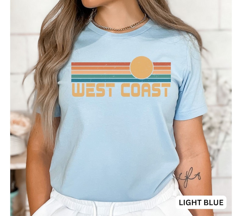 May include: Light blue t-shirt with a retro sunset graphic and the text "WEST COAST" in yellow.