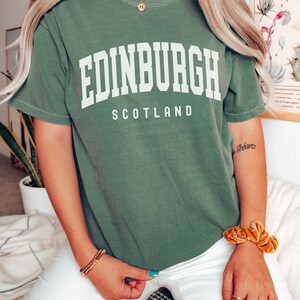 K&ouml;nnte beinhalten: Ein gr&uuml;nes T-Shirt mit dem Text "EDINBURGH SCOTLAND" in wei&szlig;en Buchstaben.