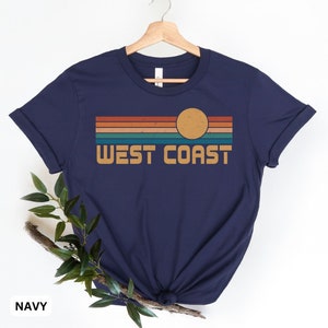 May include: A navy blue t-shirt with a retro sunset graphic and the text "WEST COAST" printed on the front.