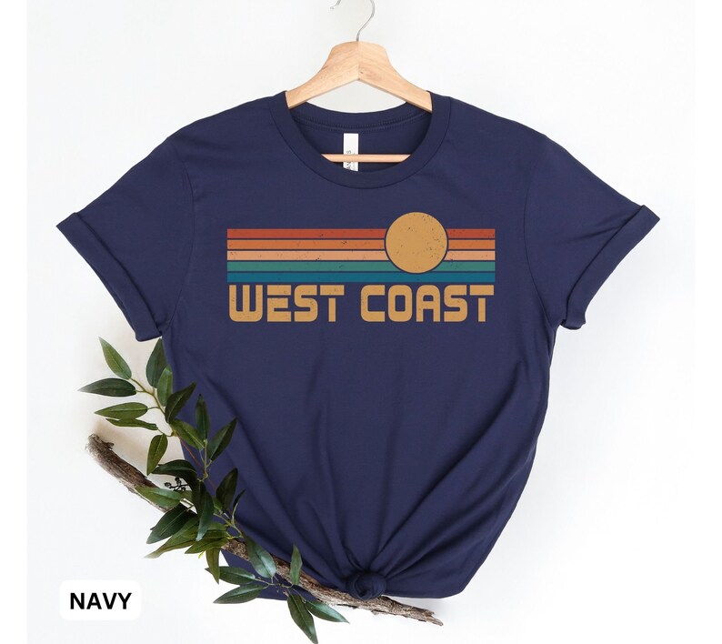 May include: A navy blue t-shirt with a retro sunset graphic and the text "WEST COAST" printed on the front.