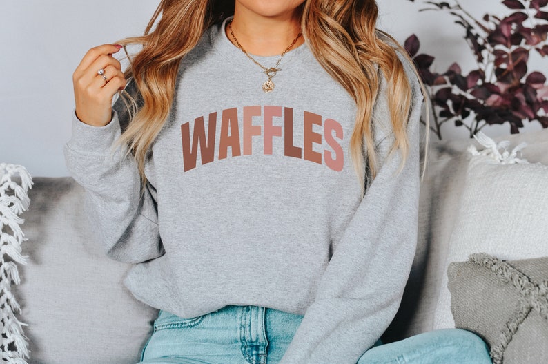 May include: A gray sweatshirt with the word "WAFFLES" printed in a rainbow of colors across the chest.