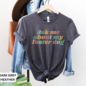 May include: Dark grey heather t-shirt with the text "Ask me about my foster dog" in colorful retro font.