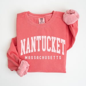 May include: A coral pink sweatshirt with the text "NANTUCKET MASSACHUSETTS" in white.
