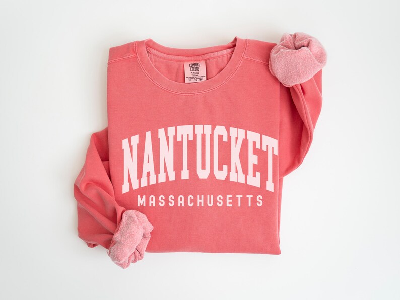 May include: A coral pink sweatshirt with the text "NANTUCKET MASSACHUSETTS" in white.
