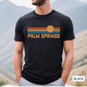 May include: A black t-shirt with a retro-style graphic of a sunset over a mountain range. The graphic includes the text "PALM SPRINGS" in white letters.