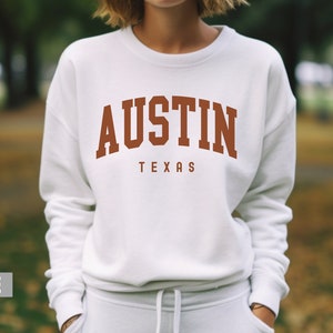 May include: White sweatshirt with a brown "AUSTIN TEXAS" graphic on the front.