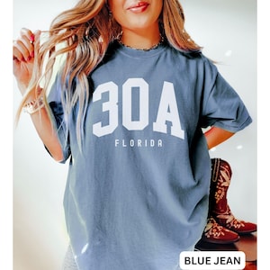 May include: A blue jean t-shirt with white text that says "30A FLORIDA" in a varsity style font.