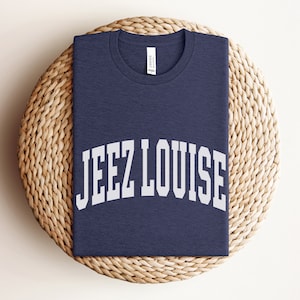 May include: A navy blue t-shirt with the text "JEEZ LOUISE" printed in white in an arched font.