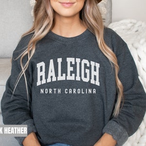 Pode incluir: Camisola de moletom cinza escuro com texto branco que diz "RALEIGH NORTH CAROLINA".