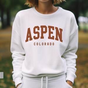 May include: White sweatshirt with a brown graphic that says "ASPEN COLORADO" in a collegiate font.