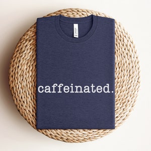 Op de afbeelding: Een marineblauw t-shirt met de tekst "caffeinated." in wit op de voorkant.