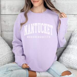 May include: A lavender sweatshirt with the text "NANTUCKET MASSACHUSETTS" in white.