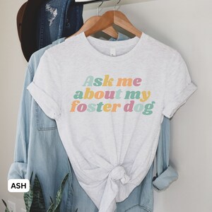 May include: A light gray t-shirt with the text "Ask me about my foster dog" in colorful retro-style lettering.