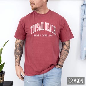 Pu&ograve; includere: T-shirt color cremisi con la scritta bianca "TOPSAIL BEACH NORTH CAROLINA". La maglietta a maniche corte sembra essere realizzata in un materiale morbido e confortevole. La parola "CRIMSON" &egrave; visualizzata in un riquadro rettangolare in basso a destra.