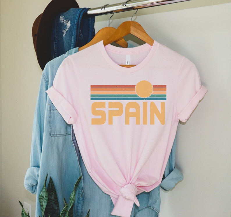 May include: A pink t-shirt with a retro sunset graphic and the word "SPAIN" in a vintage font.