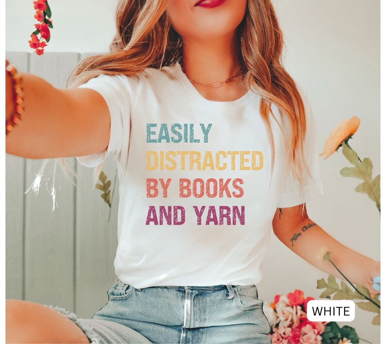 May include: White t-shirt with the text "EASILY DISTRACTED BY BOOKS AND YARN" in colorful, distressed lettering.