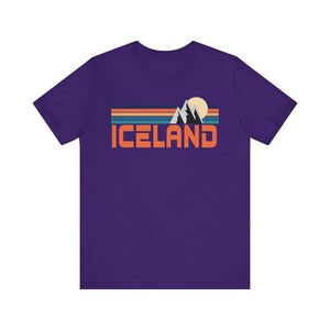 Puede incluir: Camiseta de manga corta de color morado con un gr&aacute;fico retro de monta&ntilde;as, un sol y la palabra "ICELAND" en naranja.