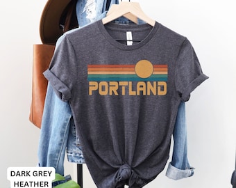 Könnte beinhalten: Dunkelgraues T-Shirt aus Heather-Material mit einem Retro-Sonnenuntergang-Motiv und dem Wort "PORTLAND" auf der Vorderseite.