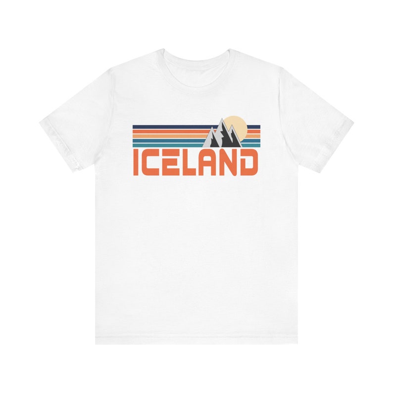 Puede incluir: Camiseta blanca con un dise&ntilde;o gr&aacute;fico retro que presenta una cordillera, un sol y la palabra "ICELAND" en naranja.