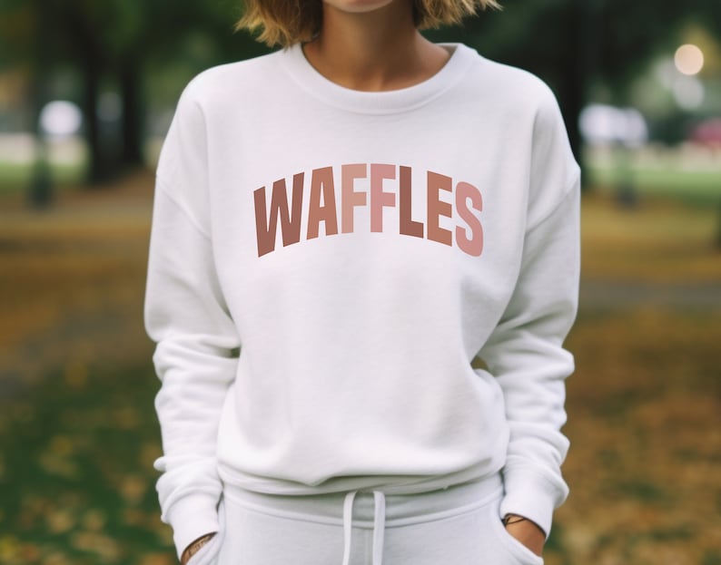May include: White sweatshirt with a pink and orange gradient text that reads "WAFFLES" on the front.