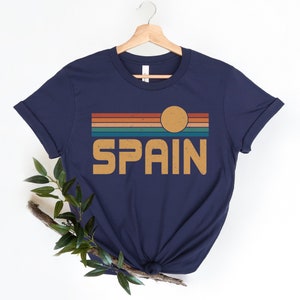 May include: A navy blue t-shirt with a retro-style graphic of a sunset over the word "SPAIN" in orange.