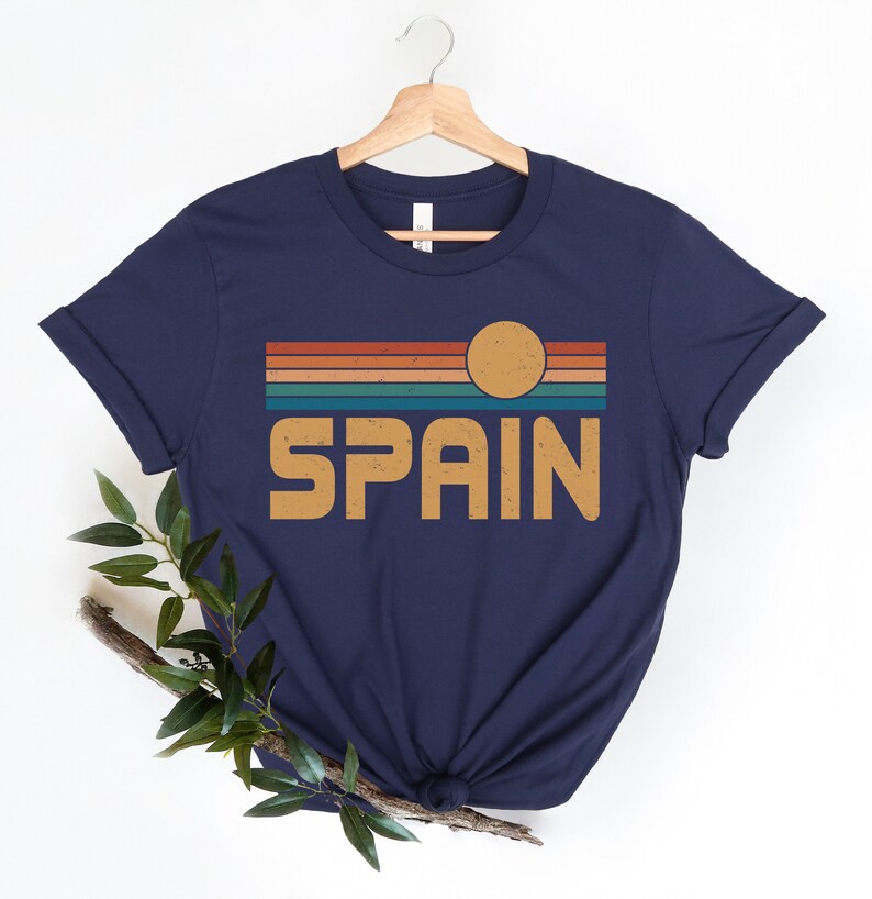 May include: A navy blue t-shirt with a retro-style graphic of a sunset over the word "SPAIN" in orange.