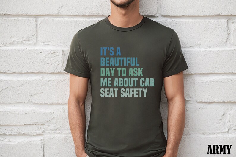 K&ouml;nnte beinhalten: Ein dunkelgr&uuml;nes T-Shirt mit einer wei&szlig;en Grafik, auf der "Es ist ein sch&ouml;ner Tag, um mich nach der Sicherheit von Autositzen zu fragen" steht.