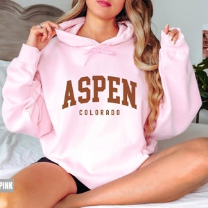 May include: A light pink hoodie with a brown arch design that says "Aspen Colorado".