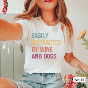 May include: White t-shirt with the text "EASILY DISTRACTED BY WINE AND DOGS" in a vintage rainbow color scheme.