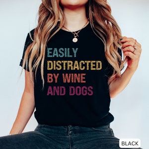 May include: Black t-shirt with the text "Easily Distracted By Wine And Dogs" in a vintage style font with colorful accents.