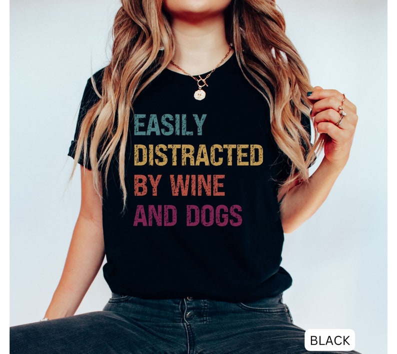 May include: Black t-shirt with the text "Easily Distracted By Wine And Dogs" in a vintage style font with colorful accents.