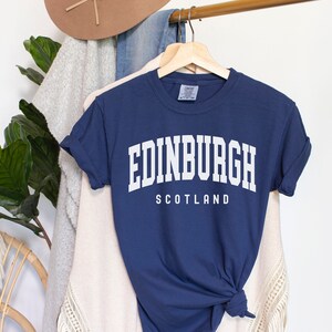 K&ouml;nnte beinhalten: Ein marineblaues T-Shirt mit wei&szlig;em Text, der "EDINBURGH SCOTLAND" lautet.