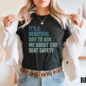 K&ouml;nnte beinhalten: Ein schwarzes T-Shirt mit dem Text "It's a beautiful day to ask me about car seat safety" in einem Farbverlauf von Blau und Gr&uuml;n.