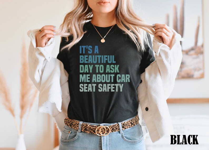K&ouml;nnte beinhalten: Ein schwarzes T-Shirt mit dem Text "It's a beautiful day to ask me about car seat safety" in einem Farbverlauf von Blau und Gr&uuml;n.